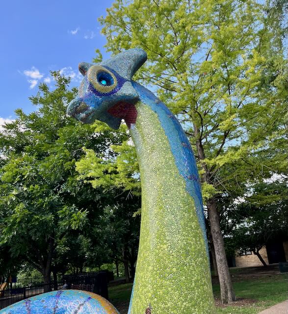 A dragon sculpture with blue glowing eyes covered in colorful glass mosaic